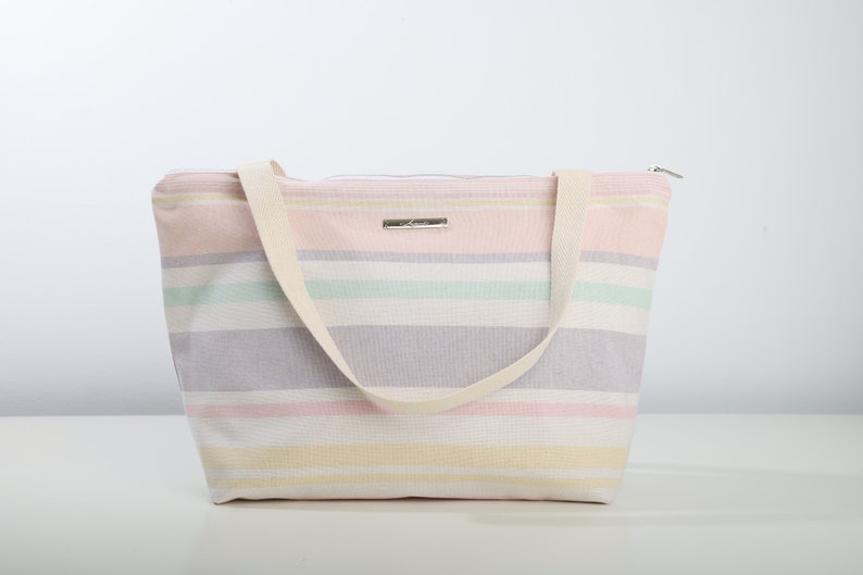 May include: A striped tote bag with a zipper closure and two fabric handles. The bag is made of a light-colored canvas with stripes of pink, yellow, green, and purple.