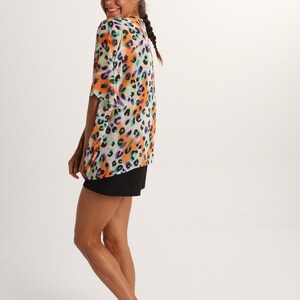 Pode incluir: Uma blusa de manga curta e corte largo com um vibrante padr&atilde;o de leopardo multicolorido em tons de laranja, roxo e turquesa sobre um fundo branco, combinada com cal&ccedil;&otilde;es pretos lisos que chegam a meio da coxa.