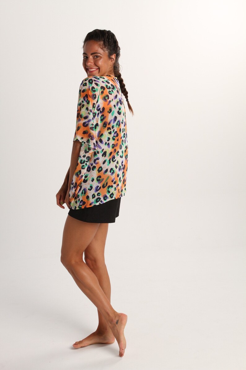 Pode incluir: Uma blusa de manga curta e corte largo com um vibrante padr&atilde;o de leopardo multicolorido em tons de laranja, roxo e turquesa sobre um fundo branco, combinada com cal&ccedil;&otilde;es pretos lisos que chegam a meio da coxa.