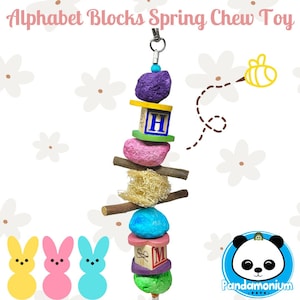 Puede incluir: Un juguete masticable de resorte con bloques de alfabeto de colores para mascotas pequeñas. El juguete presenta bloques de madera de color morado, rosa, azul y verde con las letras H y M pintadas en ellos. El juguete está encordado en una rama natural con cuerda de sisal y un clip de metal para colgar.