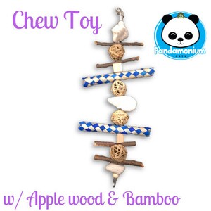 Puede incluir: Un juguete para masticar para animales pequeños, que presenta bambú tejido azul y blanco, palitos de madera de manzana y bolas de fibra natural. El juguete está colgado de una cuerda y tiene el texto "Chew Toy" y "w/ Apple wood & Bamboo" impreso en la imagen.
