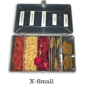 May include: A clear plastic container with six compartments, labeled "Goji Berries", "Oat Groats", "Rose Petals", "Pops", "Cookies". Each compartment contains a different type of food or ingredient, including red goji berries, oat groats, red rose petals, sticks, and green cookies.