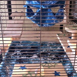 May include: A blue and white patterned fabric hammock hangs inside a cage with wooden platforms and a blue and white patterned fleece bedding.