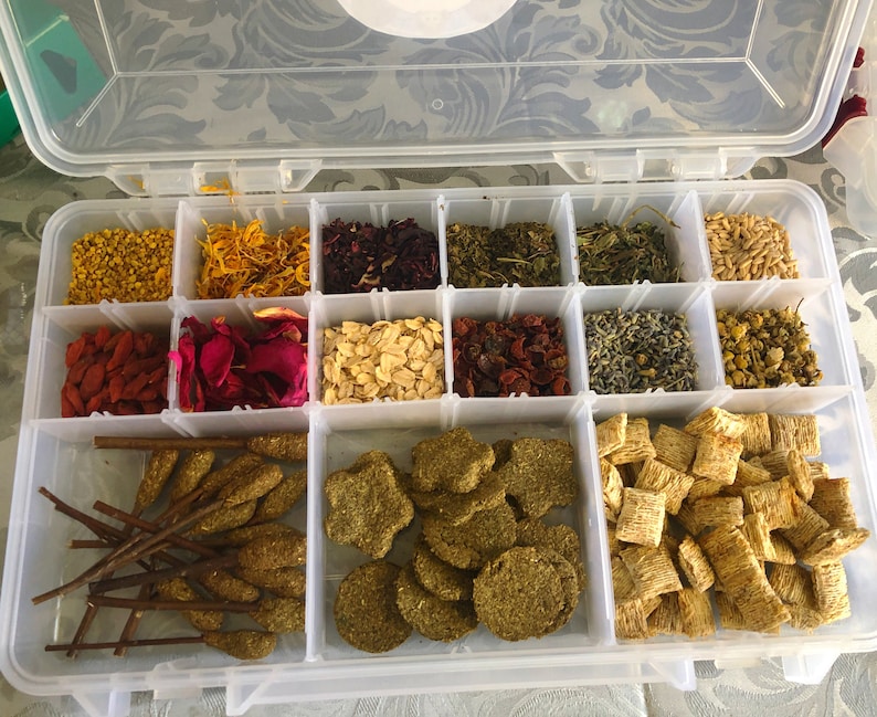 May include: A clear plastic storage container with 16 compartments filled with various dried herbs, flowers, and other ingredients. The container is open and the compartments are visible.