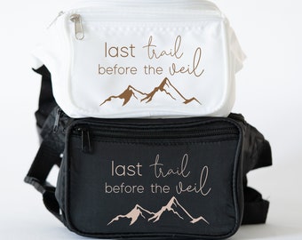 May include: Two fanny packs, one white and one black, with the text "last trail before the veil" and a mountain range graphic.
