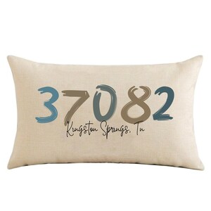May include: Beige throw pillow with the text "37082 Kingston Springs, Tn" in blue and brown paint-like lettering.