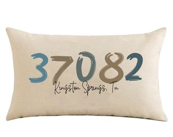 May include: Beige throw pillow with the text "37082 Kingston Springs, Tn" in blue and brown paint-like lettering.
