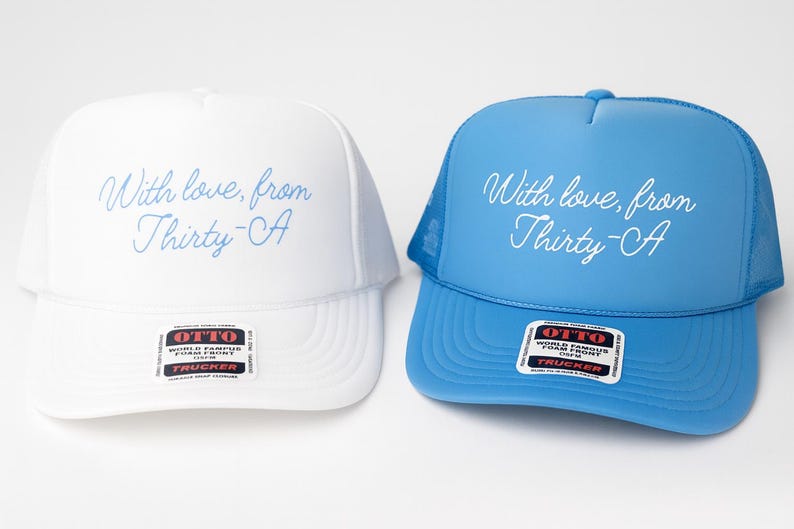 Puede incluir: Se muestran dos gorras de camionero, una blanca y otra azul claro. Ambas gorras tienen el texto "With love, from Thirty-CA" en cursiva. La gorra blanca tiene un panel frontal blanco, y la azul un panel azul. Ambas tienen una parte trasera de malla.
