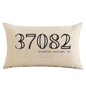 May include: Beige throw pillow with black text that reads "37082 kingston springs, tn".