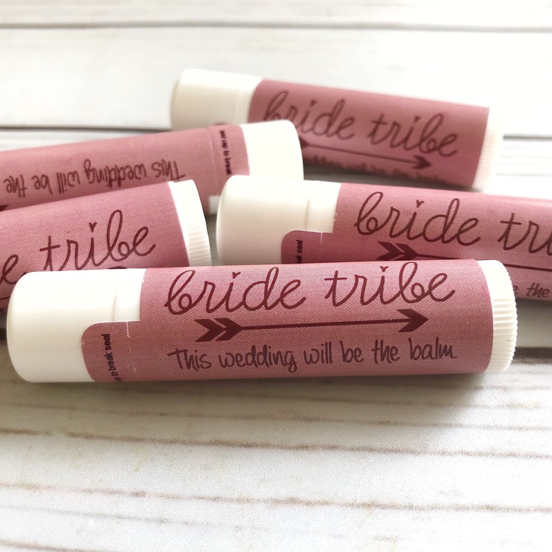 May include: A stack of pink lip balm tubes with the text "bride tribe" and "This wedding will be the balm." printed on the labels.