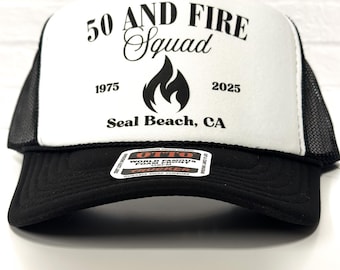 Puede incluir: Gorra de camionero en blanco y negro con el texto "50 AND FIRE Squad" y un gráfico de llama. La gorra también incluye los años "1975" y "2025" y la ubicación "Seal Beach, CA".