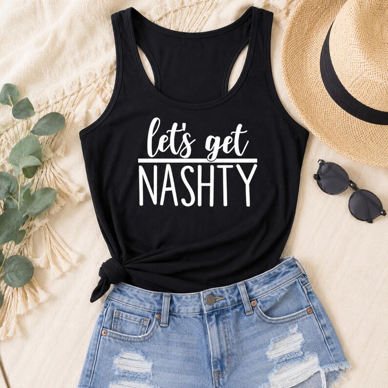 May include: A black racerback tank top featuring the white text "let's get NASHTY" printed on the front. The garment has a scoop neckline and a knotted detail at the bottom hem, paired with light blue distressed denim shorts.