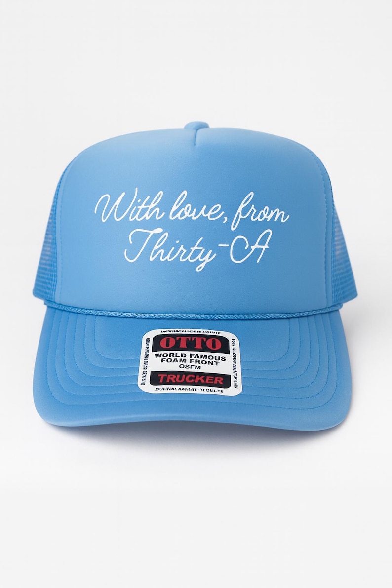 Puede incluir: Gorra de camionero azul claro con parte trasera de malla y visera curva. La gorra presenta el texto "With love, from Thirty-A" en escritura blanca. La parte delantera de la gorra tiene una etiqueta blanca que dice "OTTO WORLD FAMOUS FOAM FRONT OSFM TRUCKER".