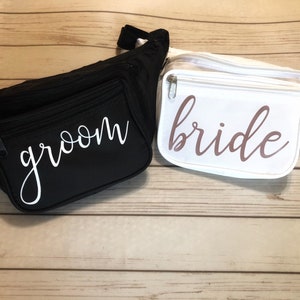 Puede incluir: Dos riñoneras, una negra con la palabra "groom" en letras blancas y una blanca con la palabra "bride" en letras rosas.