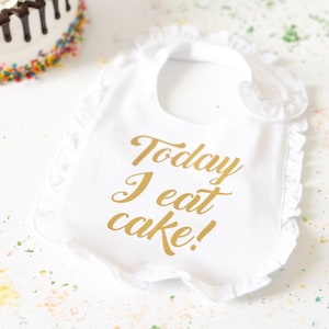 May include: White bib with a gold inscription that reads "Today I eat cake!"