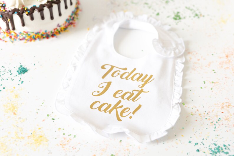 May include: White bib with a gold inscription that reads "Today I eat cake!"