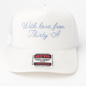 Puede incluir: Gorra de camionero blanca con parte trasera de malla y frontal de espuma. La gorra presenta el texto "With love, from Thirty-CA" en escritura azul. Una etiqueta indica "OTTO" y "TRUCKER".