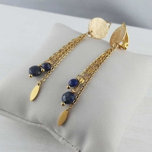 Può includere: Orecchini a clip dorati con un disco rotondo testurizzato e più catene con perline di lapislazzuli blu.