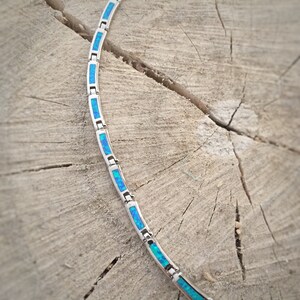 May include: A silver necklace with rectangular blue opal inlays. The necklace is displayed on a weathered wooden surface, showcasing the jewelry's design and color contrast. The opal inlays have a vibrant blue hue.