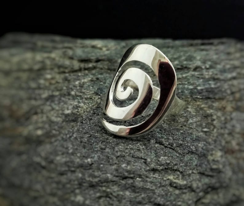 May include: A silver ring with a spiral design. The ring is made of a smooth, shiny metal and has a simple, elegant look.