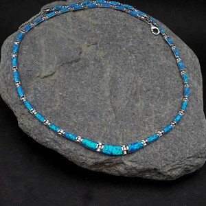 Puede incluir: Un collar de plata con eslabones de &oacute;palo azul. El collar est&aacute; sobre un fondo de roca gris.