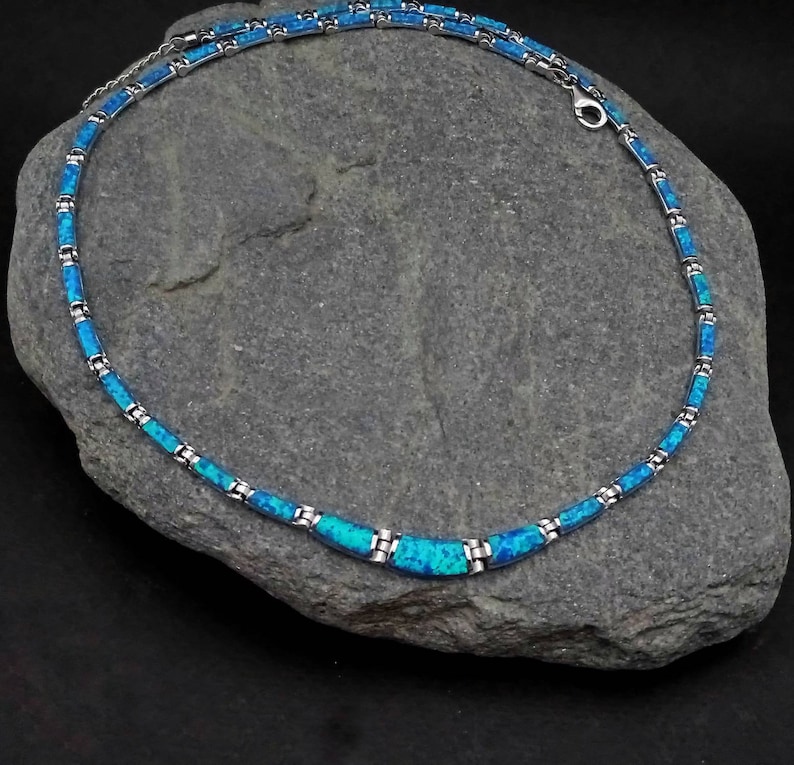 Puede incluir: Un collar de plata con eslabones de &oacute;palo azul. El collar est&aacute; sobre un fondo de roca gris.