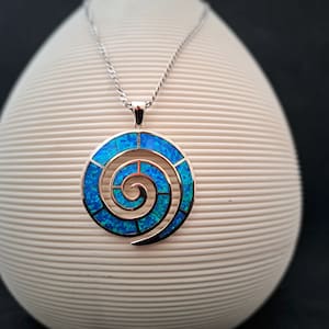 May include: A silver necklace with a blue opal spiral pendant. The pendant is a circular design with a spiral pattern made of small blue opal pieces.
