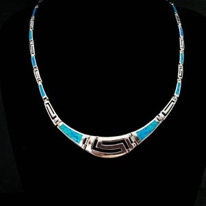 May include: A silver necklace with a blue opal inlay in a geometric pattern. The necklace is made of sterling silver and features a unique design.