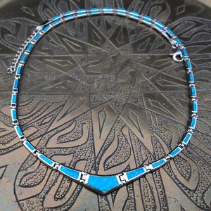 May include: A silver-toned necklace with turquoise-colored rectangular and triangular inlays. The necklace has a delicate chain and a secure clasp. The design features a V-shaped pendant at the center, creating a striking visual appeal.