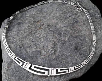 May include: A silver necklace with a geometric pattern. The necklace is made of interlocking squares and rectangles, creating a Greek key design.