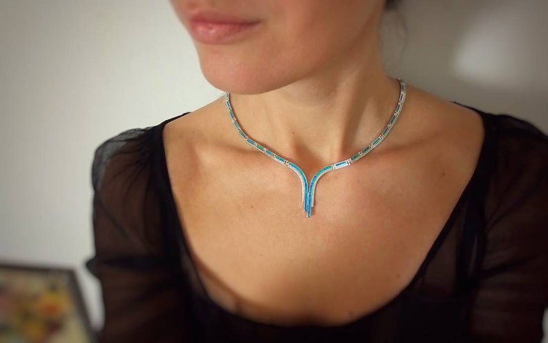 Peut inclure: Un collier en argent avec un pendentif en forme de V serti de pierres turquoise.