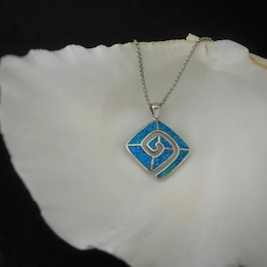 May include: A silver pendant necklace featuring a square pendant with a blue opal inlay and a spiral design. The necklace is displayed on a white surface against a black background. The pendant is approximately 1 inch square.