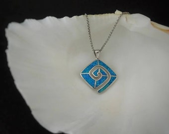 Könnte beinhalten: Eine silberne Halskette mit Anhänger, quadratisch. Der Anhänger hat einen blauen Opal-Inlay und ein Spiraldesign. Die Halskette wird auf einer weißen Oberfläche vor schwarzem Hintergrund präsentiert. Der Anhänger ist ca. 2,5 cm groß.