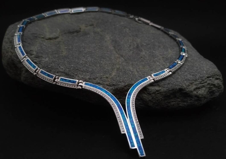 Peut inclure: Un collier en argent avec un motif en opale bleue. Le collier a un pendentif en forme de Y avec un motif g&eacute;om&eacute;trique.