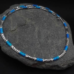 May include: A silver chain necklace with blue opal beads and a Greek key design.