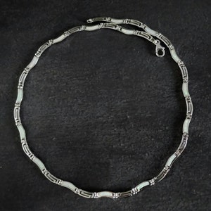 May include: A silver chain necklace with white enamel accents. The chain is made of small, linked ovals.