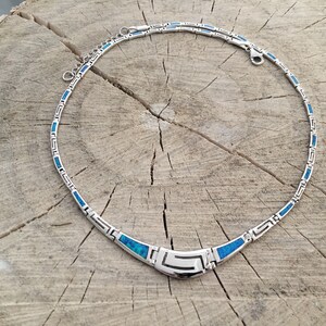 May include: A silver necklace with a blue opal inlay. The necklace has a geometric design and a clasp closure.