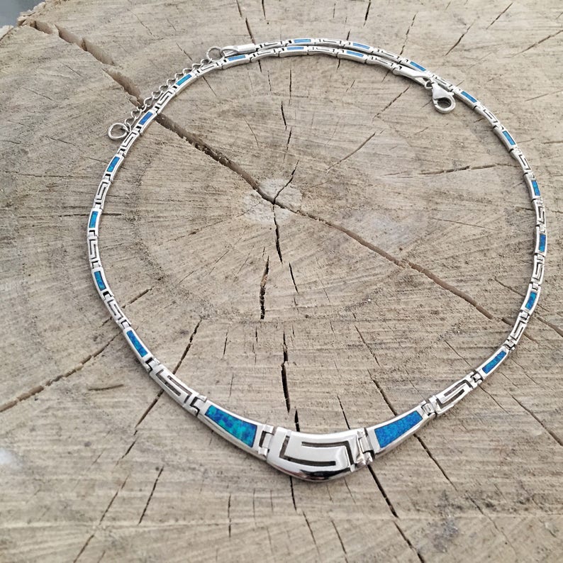 May include: A silver necklace with a blue opal inlay. The necklace has a geometric design and a clasp closure.