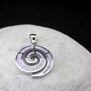 May include: A silver pendant with a spiral design. The pendant features a light purple and white opal inlay, set within a polished silver frame. The spiral design is a prominent feature, creating a visually appealing and intricate pattern. The pendant is designed to be worn as a necklace.