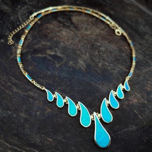 May include: A gold-toned necklace with a series of turquoise teardrop-shaped pendants. The necklace has a delicate chain and a decorative design along the collar. The teardrop pendants are graduated in size, with the largest at the center.