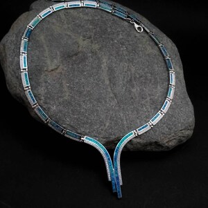 Peut inclure: Un collier en argent avec une incrustation d'opale bleue et verte. Le collier a un pendentif en forme de V avec deux brins.