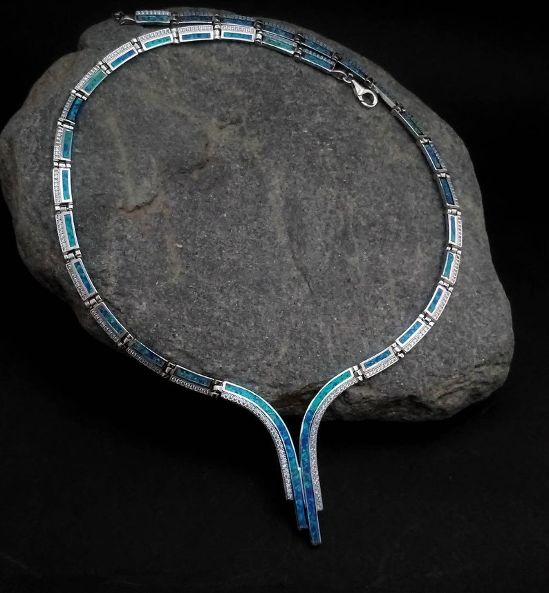 Peut inclure: Un collier en argent avec une incrustation d'opale bleue et verte. Le collier a un pendentif en forme de V avec deux brins.