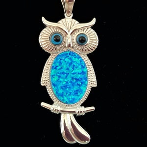 K&ouml;nnte beinhalten: Silberner Eulens Anh&auml;nger mit blauen Opal-Steinen als Augen. Die Eule sitzt auf einem Ast mit ausgebreiteten Fl&uuml;geln.