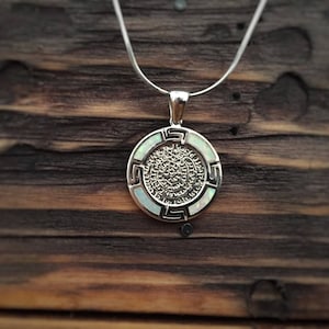 May include: A silver necklace with a white opal pendant featuring a detailed circular design with a Greek key border.