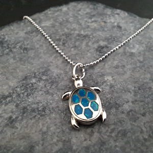 Op de afbeelding: Een zilveren ketting met een zilveren schildpad hanger. De schildpad heeft een schild van blauwe opaal stenen.