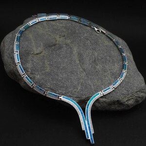Peut inclure: Un collier en argent avec un pendentif en opale bleue. Le collier est compos&eacute; de petits maillons rectangulaires et pr&eacute;sente un design d&eacute;licat et &eacute;l&eacute;gant.