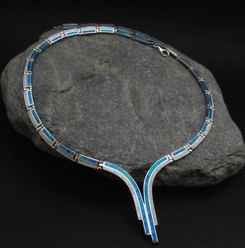 Peut inclure: Un collier en argent avec un pendentif en opale bleue. Le collier est compos&eacute; de petits maillons rectangulaires et pr&eacute;sente un design d&eacute;licat et &eacute;l&eacute;gant.