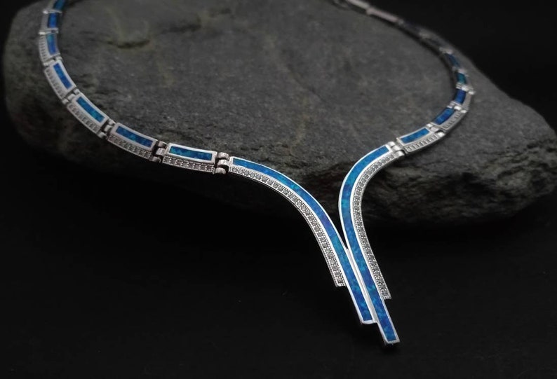 Peut inclure: Un collier en argent avec un motif en opale bleue. Le collier est compos&eacute; de pi&egrave;ces d'argent reli&eacute;es entre elles avec des incrustations d'opale bleue. Le collier a un pendentif en forme de V avec un motif en opale bleue.