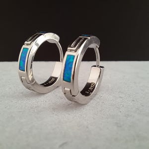 Op de afbeelding: Een paar zilveren creolen met blauwe opaal-inleg. De oorbellen zijn gemarkeerd met "0.1 79925".