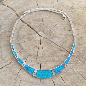 Può includere: Una collana color argento caratterizzata da una serie di segmenti intarsiati di un blu vibrante e iridescente, disposti in un design curvo a girocollo. Le maglie della catena presentano un motivo geometrico a chiave greca e una chiusura a moschettone.